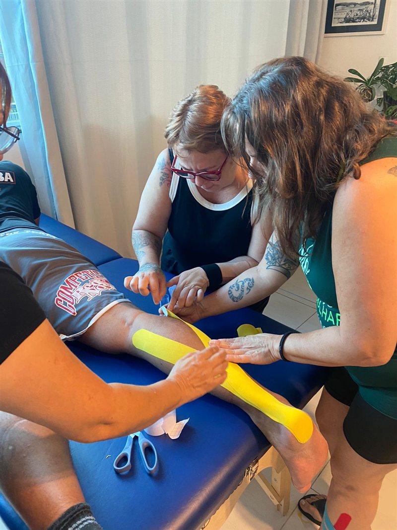 Alunas aplicando kinesiotape na perna de um colega