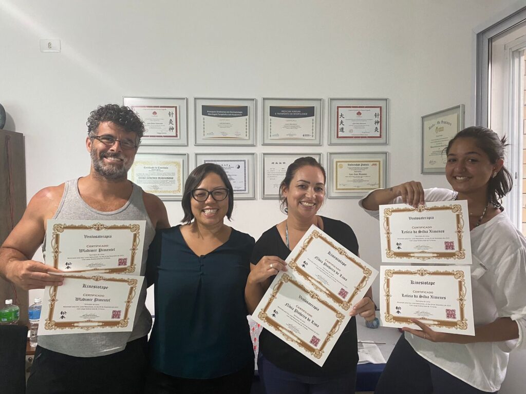 Turma com os certificados, diante da parede de formações da Dra. Luize